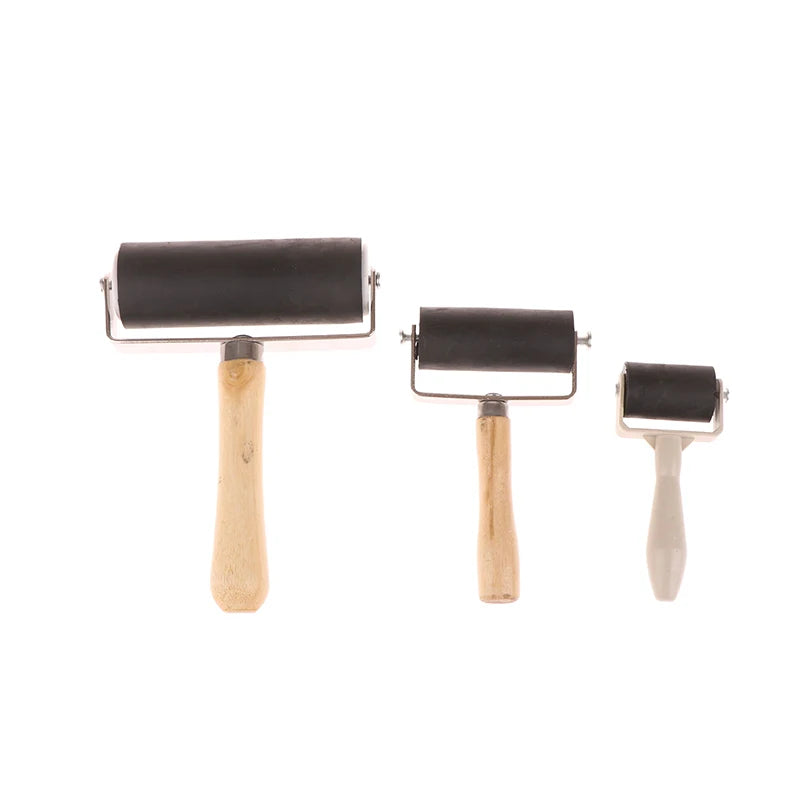 Set of three black rubber brayer rollers in large, medium, and small sizes with wooden and plastic handles.