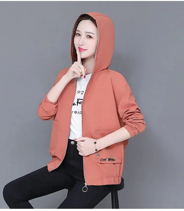 Woman wearing a terracotta-coloured hooded zip-up bomber jacket with elasticated cuffs and front pockets.