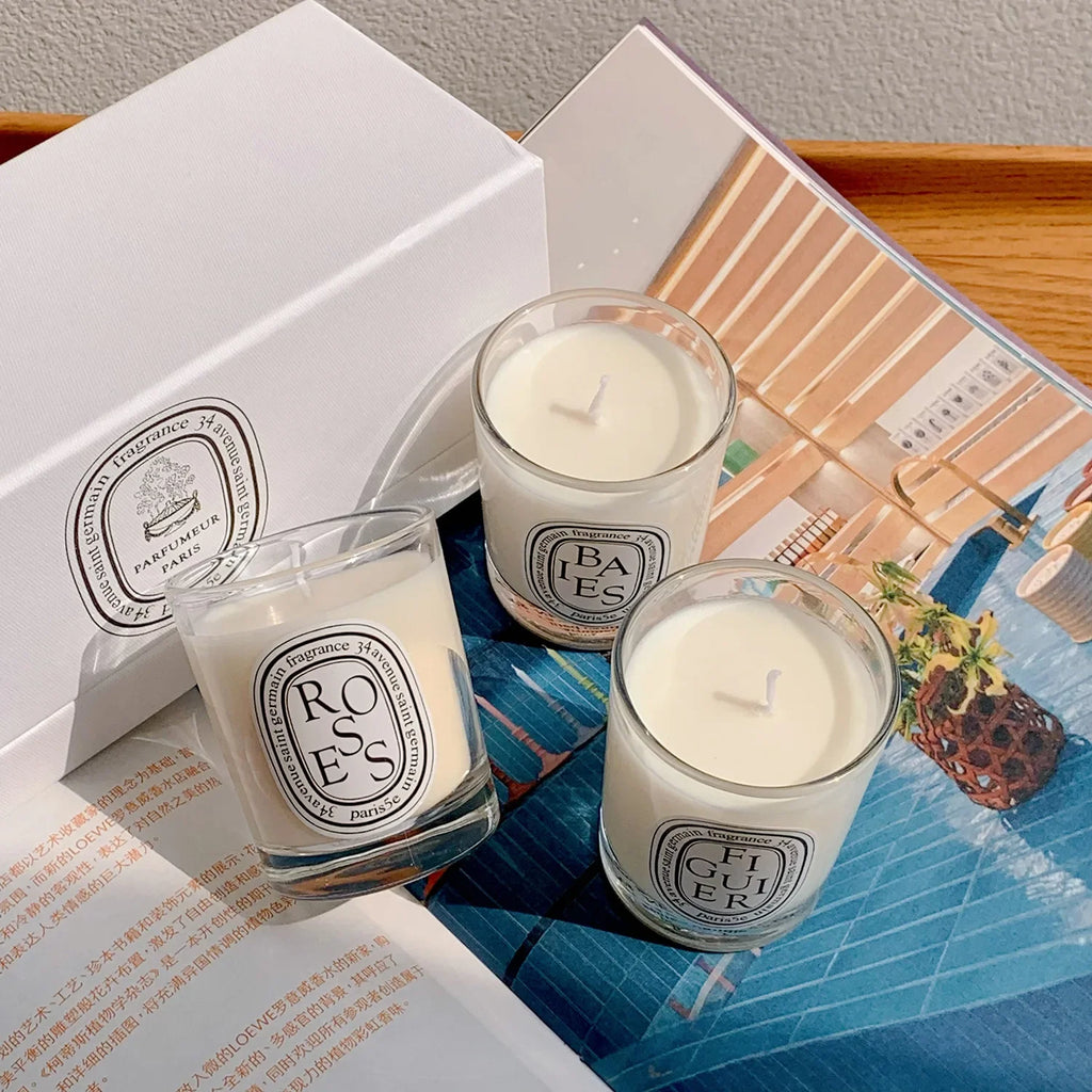 Three clear glass scented candles with white wax and iconic oval black-and-white labels, displayed with a gift box.