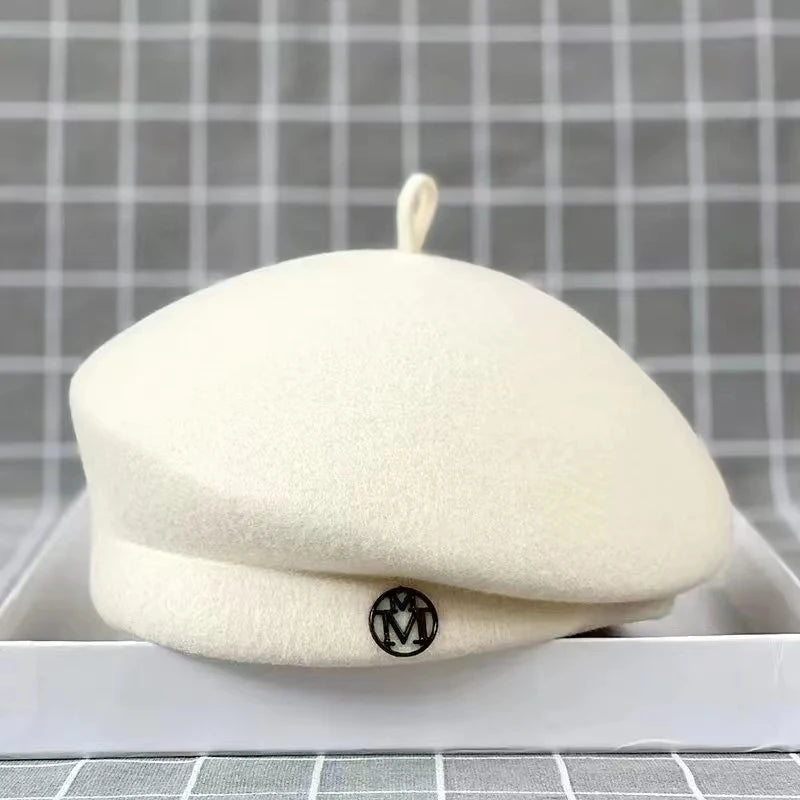 A classic cream-coloured wool felt beret with a small, circular metallic detail on the front.