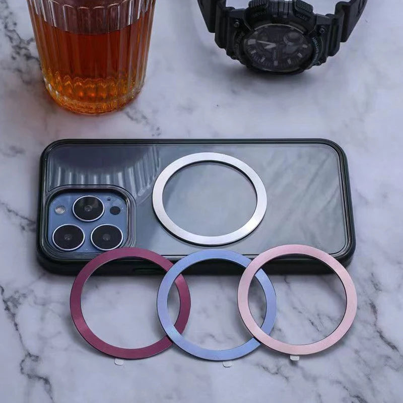 Phone case with magnetic ring, plus three extra metallic rings in dark red, blue, and pink on a marble surface.