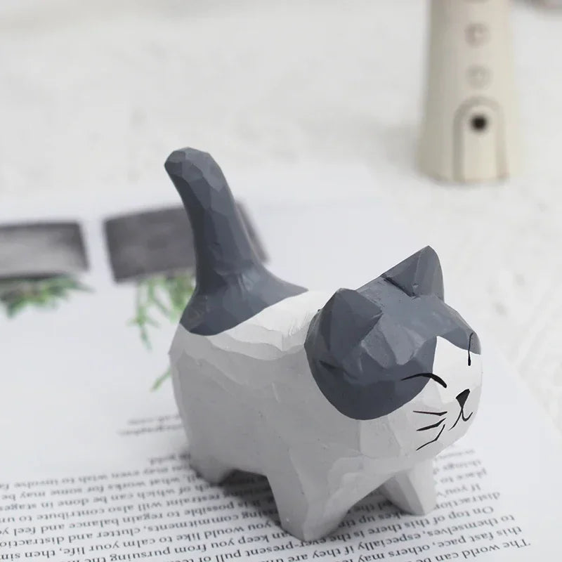 Small, grey and white hand-carved wooden cat figurine with a smiling face and playful, upright tail.