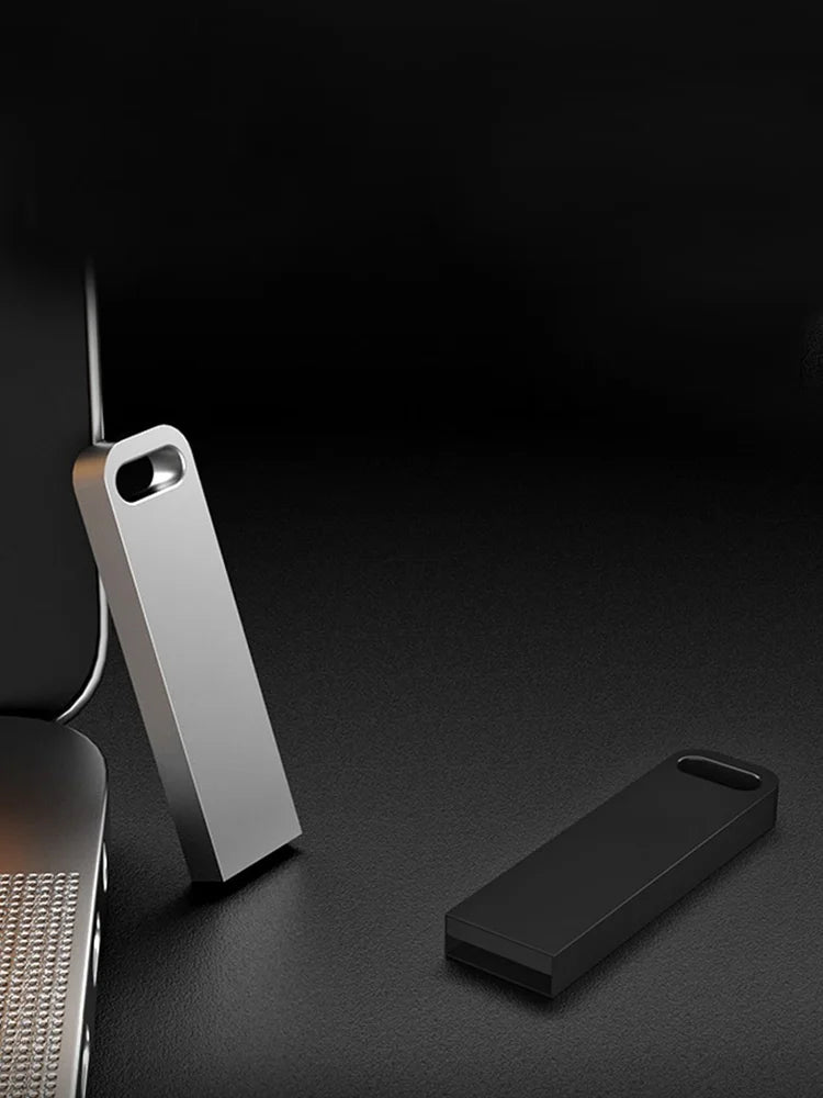 Sleek silver and black metal USB flash drives with a minimalist design and keyring hole, set on a dark surface.