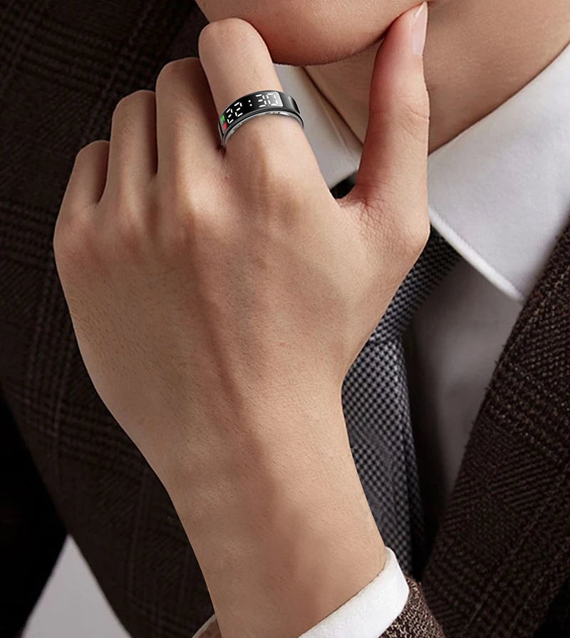 Sleek black smart health tracker ring with a glowing digital display, worn on a hand against a professional suit.