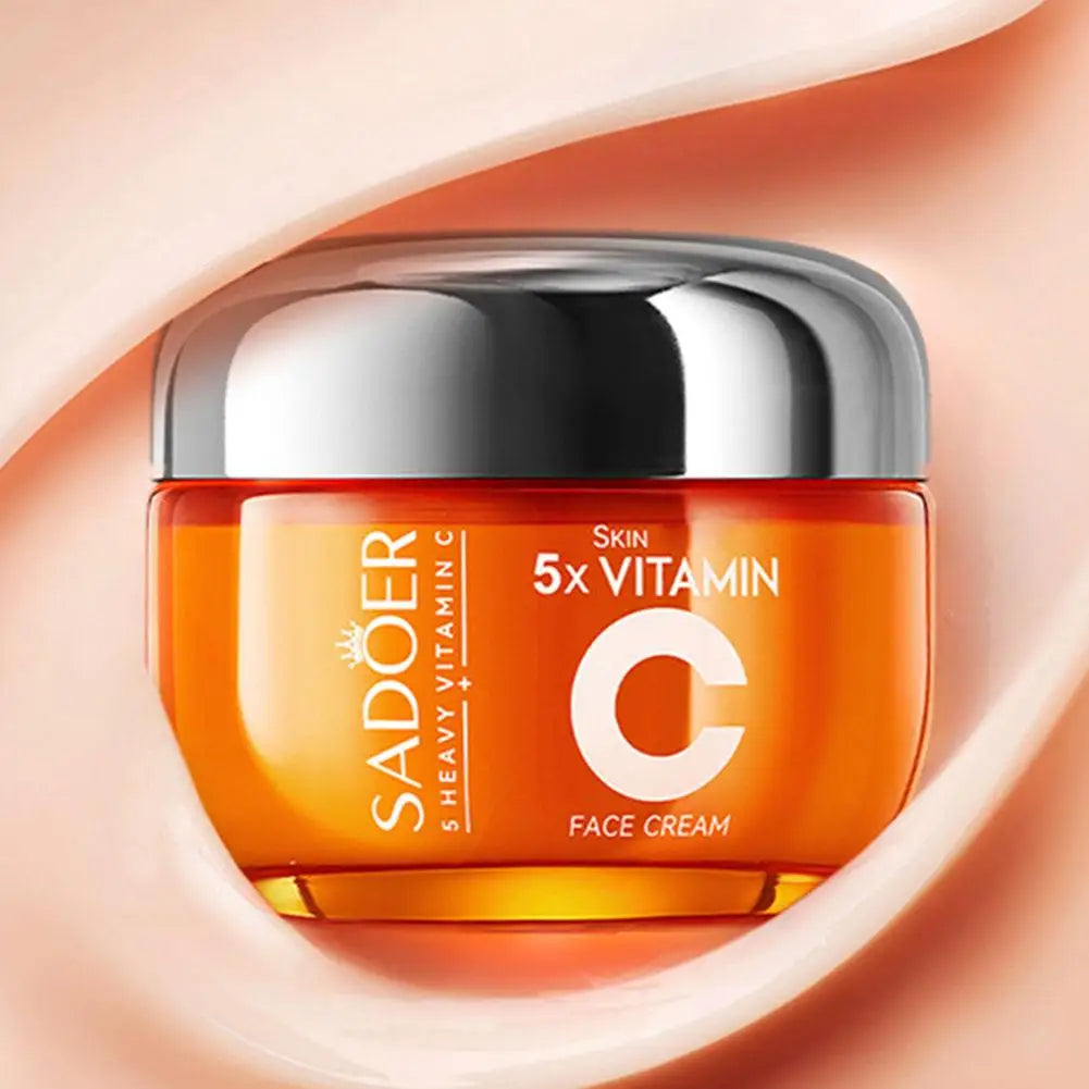 Orange jar of 5x Vitamin C face cream with a silver lid, set against a soft, creamy peach-toned background.