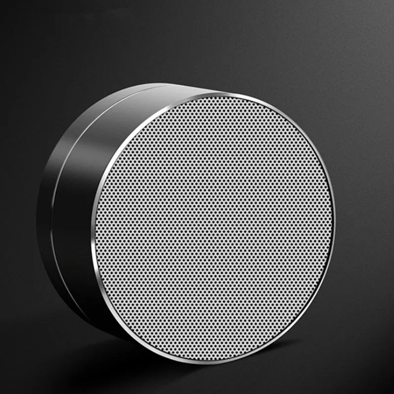 Circular, silver aluminium portable Bluetooth speaker with a metallic finish and a fine mesh front grille.