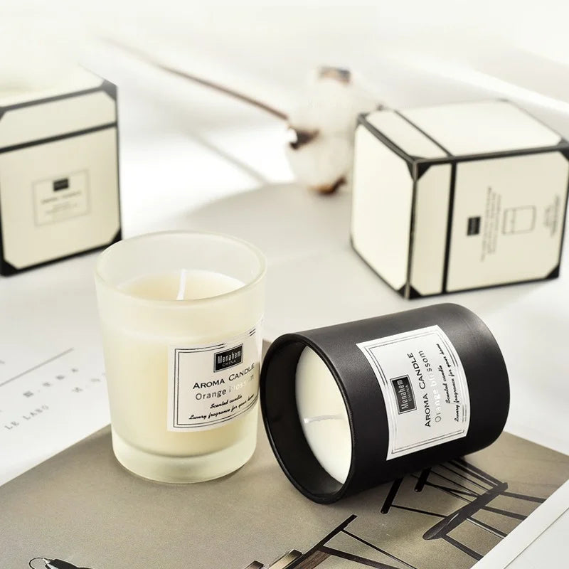 Two scented candles with orange blossom labels; one in a frosted glass jar, one in a matte black container.