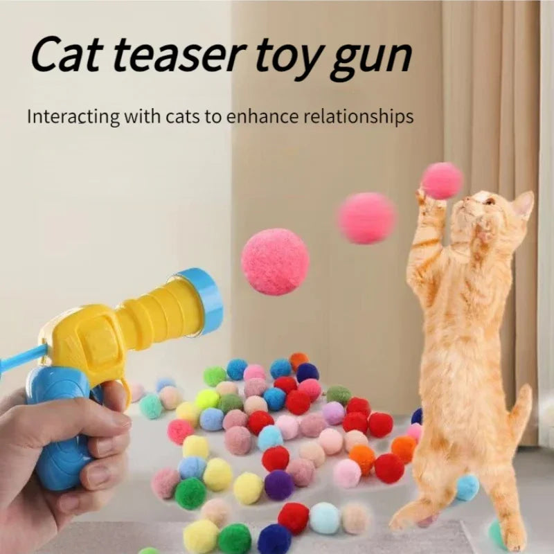 A hand holds a yellow and blue toy gun shooting colourful, soft pom-pom balls for a ginger cat to catch.