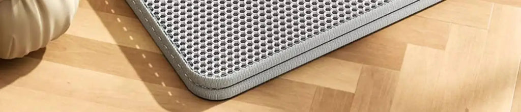 Grey, heavy-duty waterproof cat litter mat with a honeycomb trap design, sitting on a wooden floor.