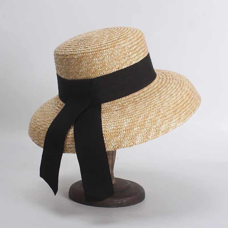 Elegant natural straw sun hat with a wide brim and a black ribbon tied in a bow at the back.