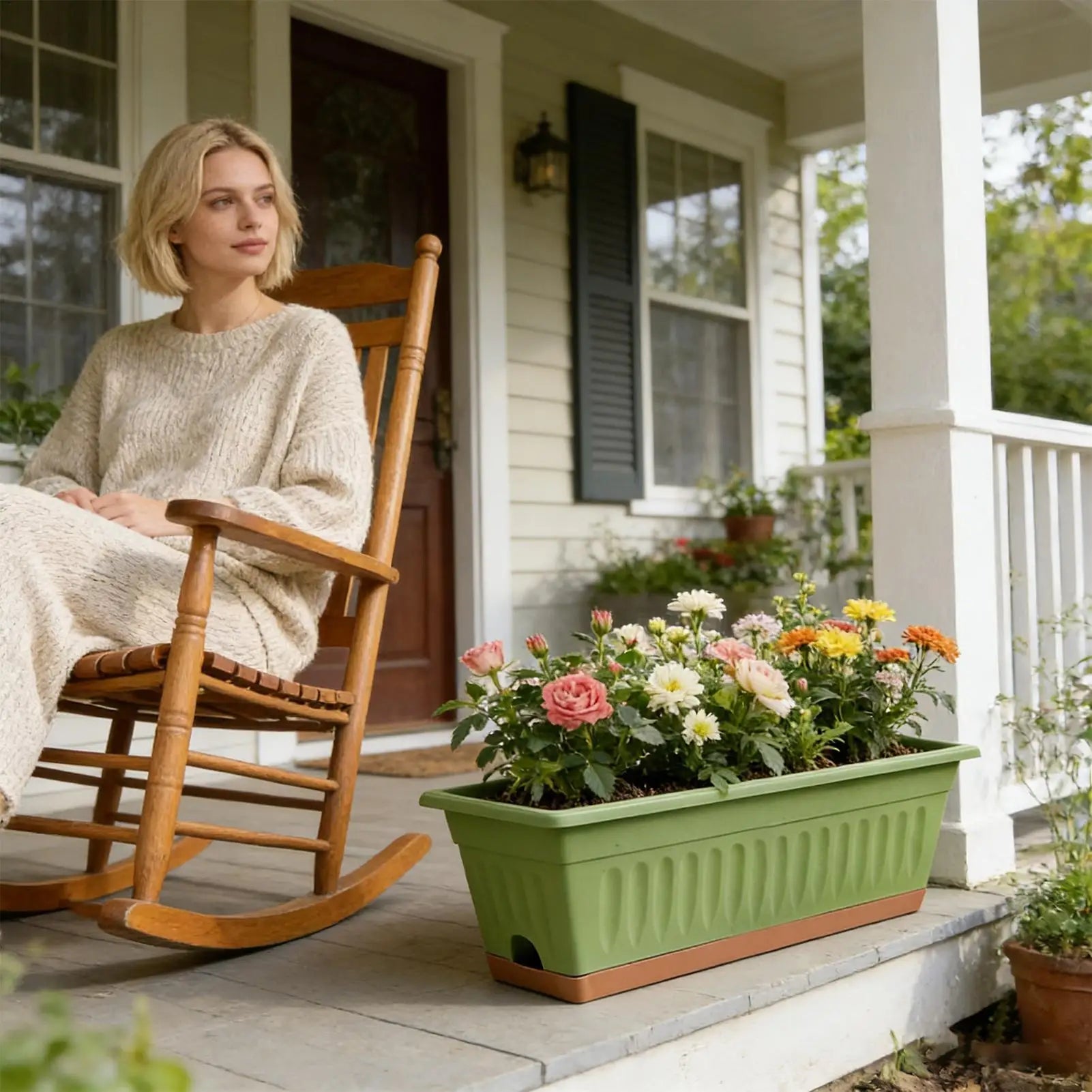 A woman sits on a porch next to a ribbed, rectangular olive green planter filled with colorful blooming flowers.
