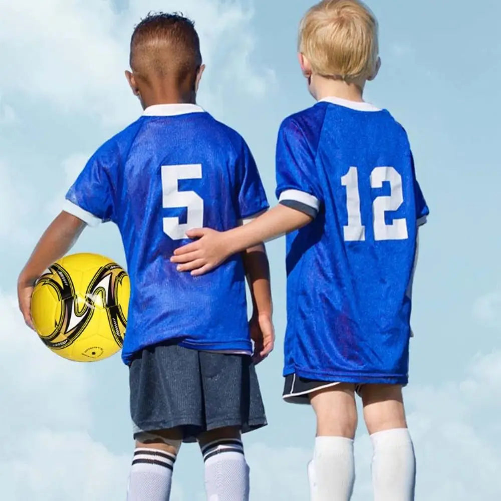 Two boys in blue football kits with numbered shirts holding a bright yellow and black football against a blue sky.