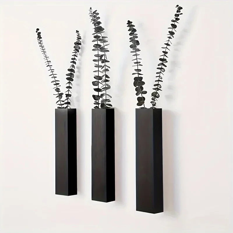 Three minimalist dark wood rectangular wall-mounted vases, each holding a decorative dried eucalyptus stem.