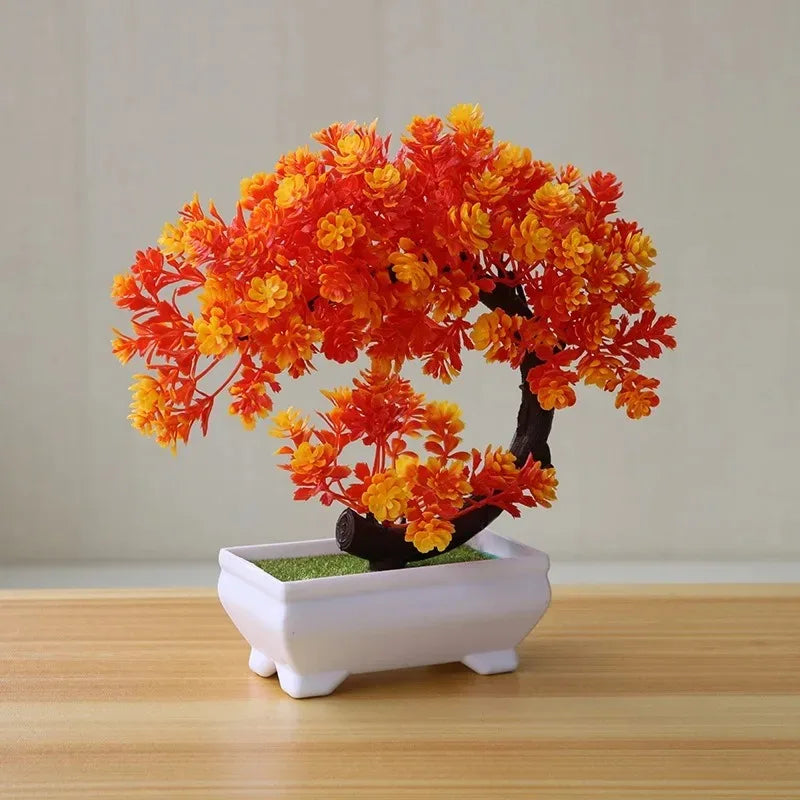 Artificial bonsai tree with vibrant red and yellow leaves in a small rectangular white pot on a wooden table.
