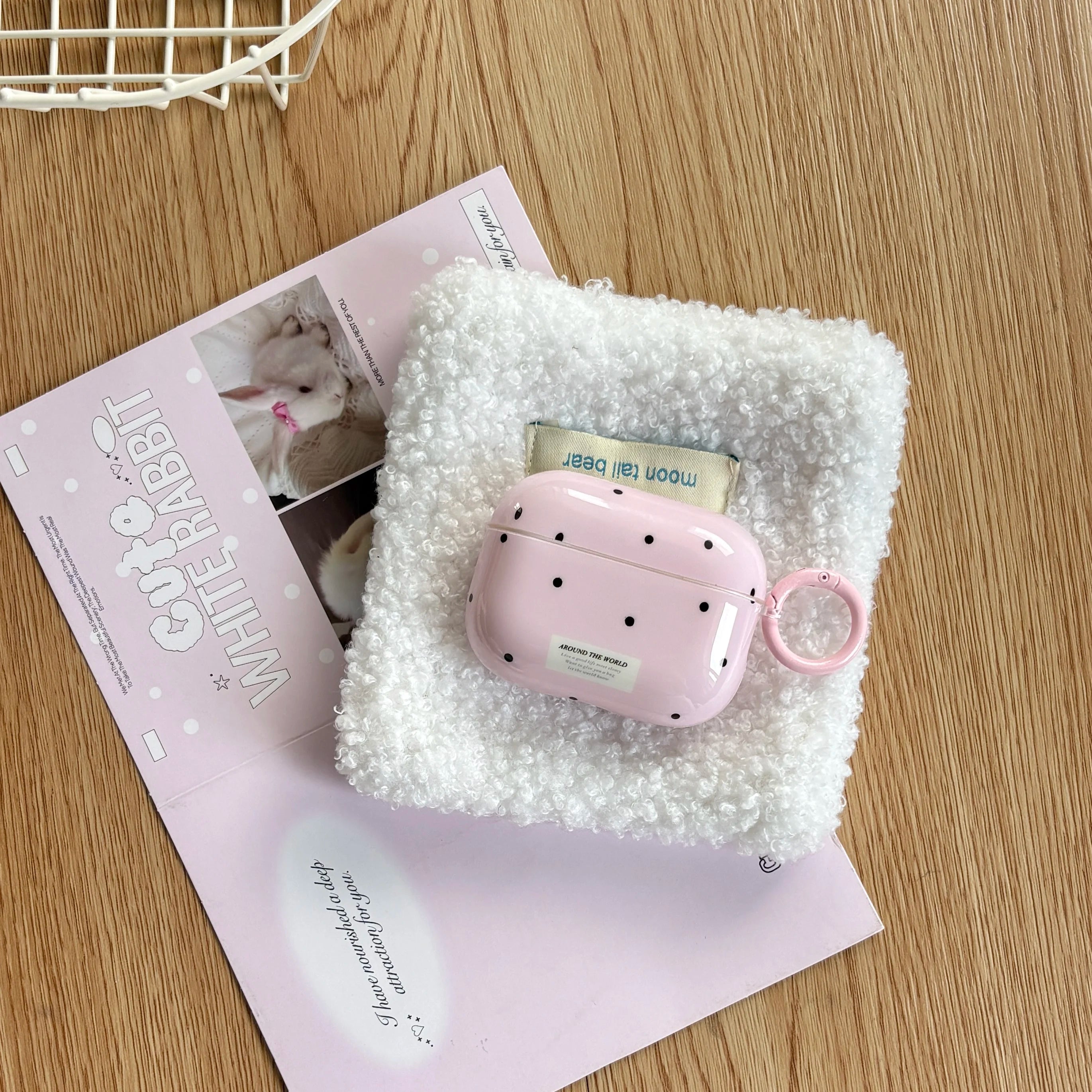 Glossy pink polka-dot AirPods Pro case with ring attachment, sitting on a white textured square fabric piece.