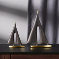 Two abstract sailboat ornaments with brushed bronze-tone sails and polished gold-tone bases on a dark surface.