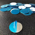 A pile of small, round, silver mirror stickers with blue protective film, some showing adhesive backs.
