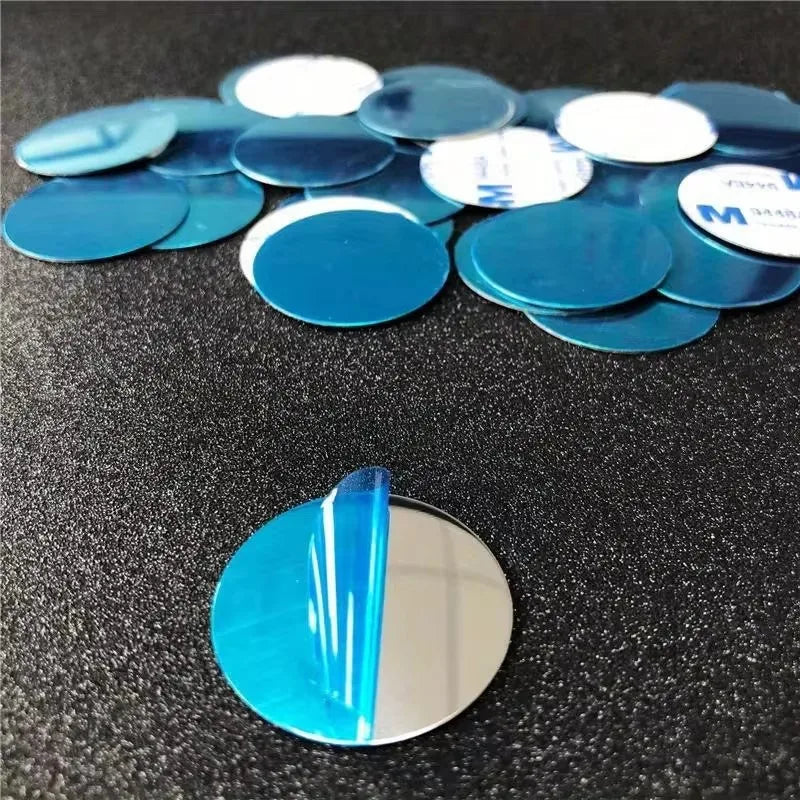 A pile of small, round, silver mirror stickers with blue protective film, some showing adhesive backs.