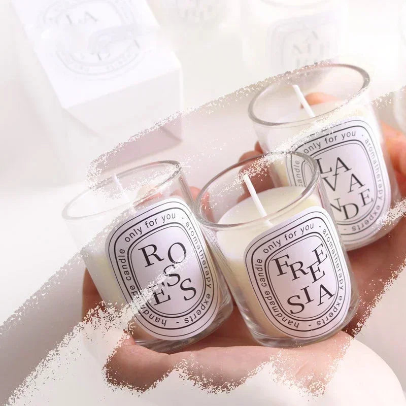 Three small aromatherapy candles in glass jars with elegant circular white labels, held in hand.
