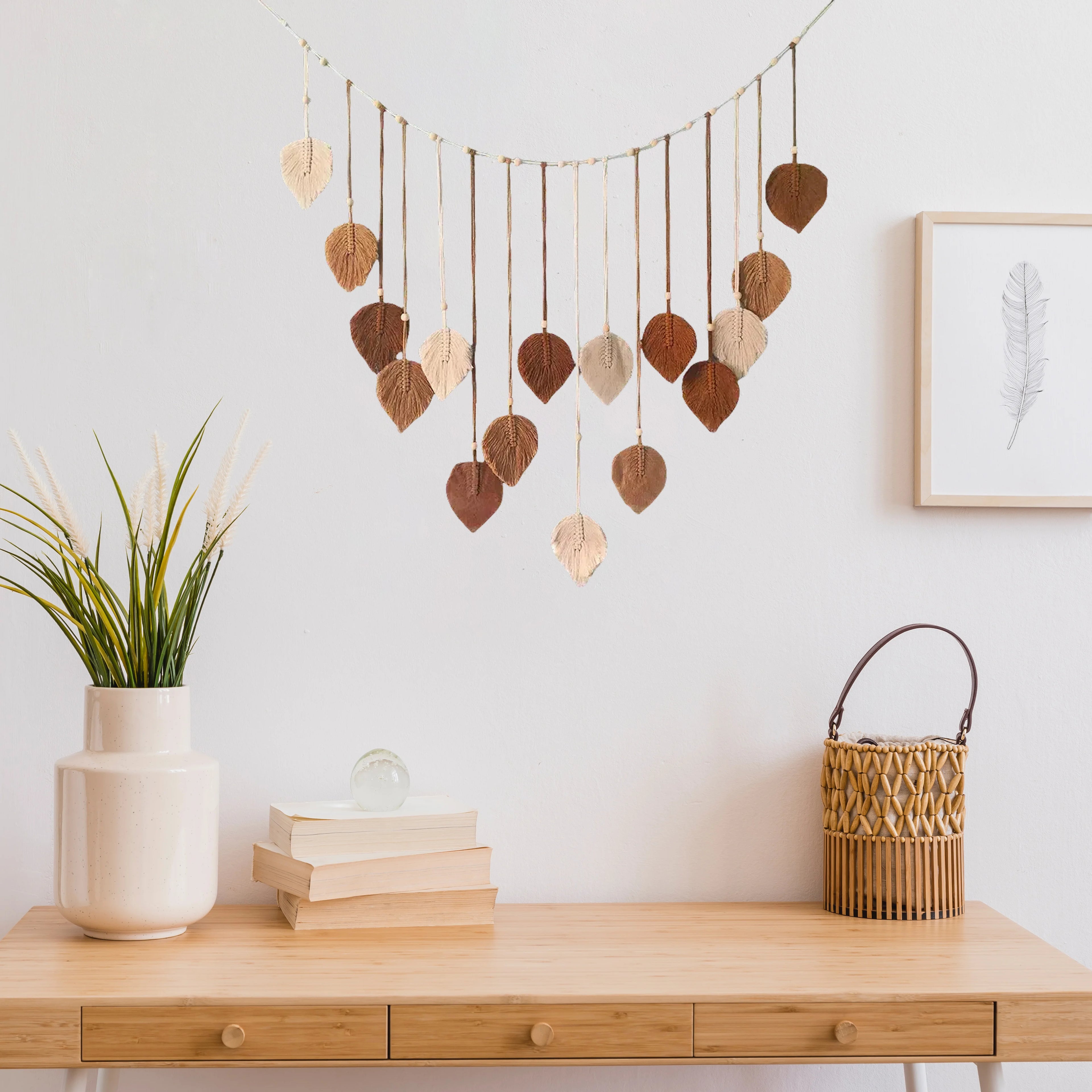 Boho-style macrame wall hanging with hanging leaf ornaments in shades of cream, tan, and brown against a white wall.