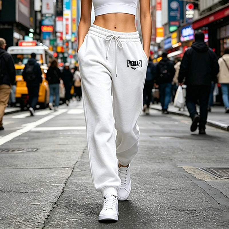 Woman wearing white high-waisted joggers with a drawstring waist and elasticated cuffs in an urban street setting.