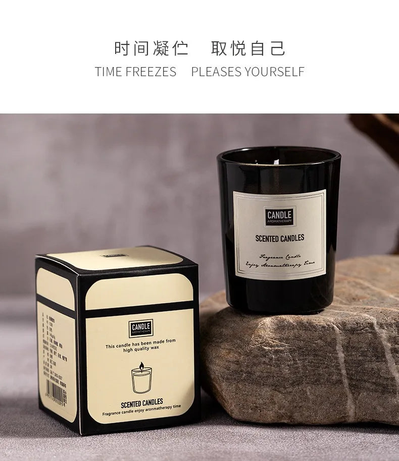 Black glass scented candle with cream and black gift box, displayed on a textured stone surface.