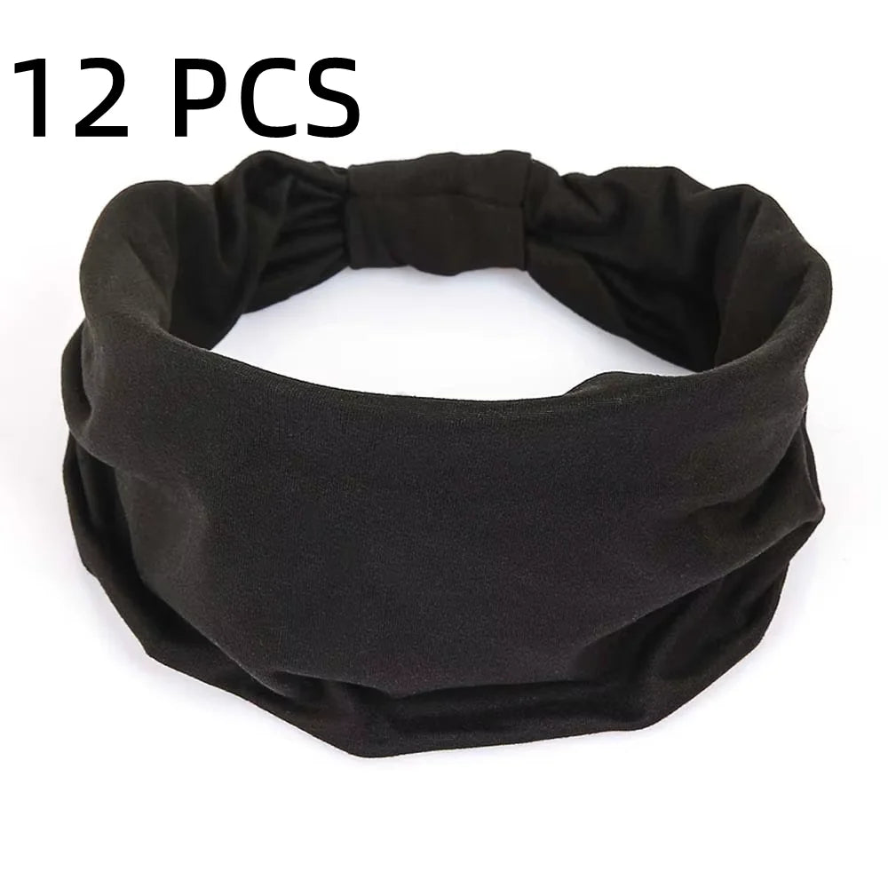 A pack of 12 plain black fabric headbands with a wide, elasticated design.