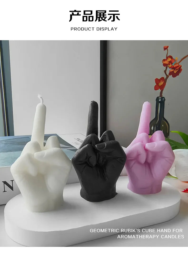 Three decorative hand-shaped candles in white, black, and pink, showing a middle-finger gesture on an oval tray.