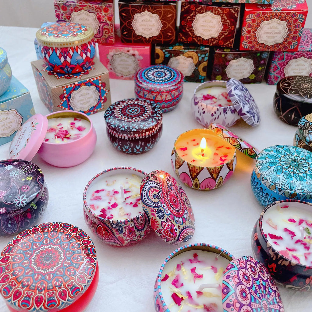 Assorted scented candles in colorful patterned metal tins with decorative floral petal wax and matching lids.
