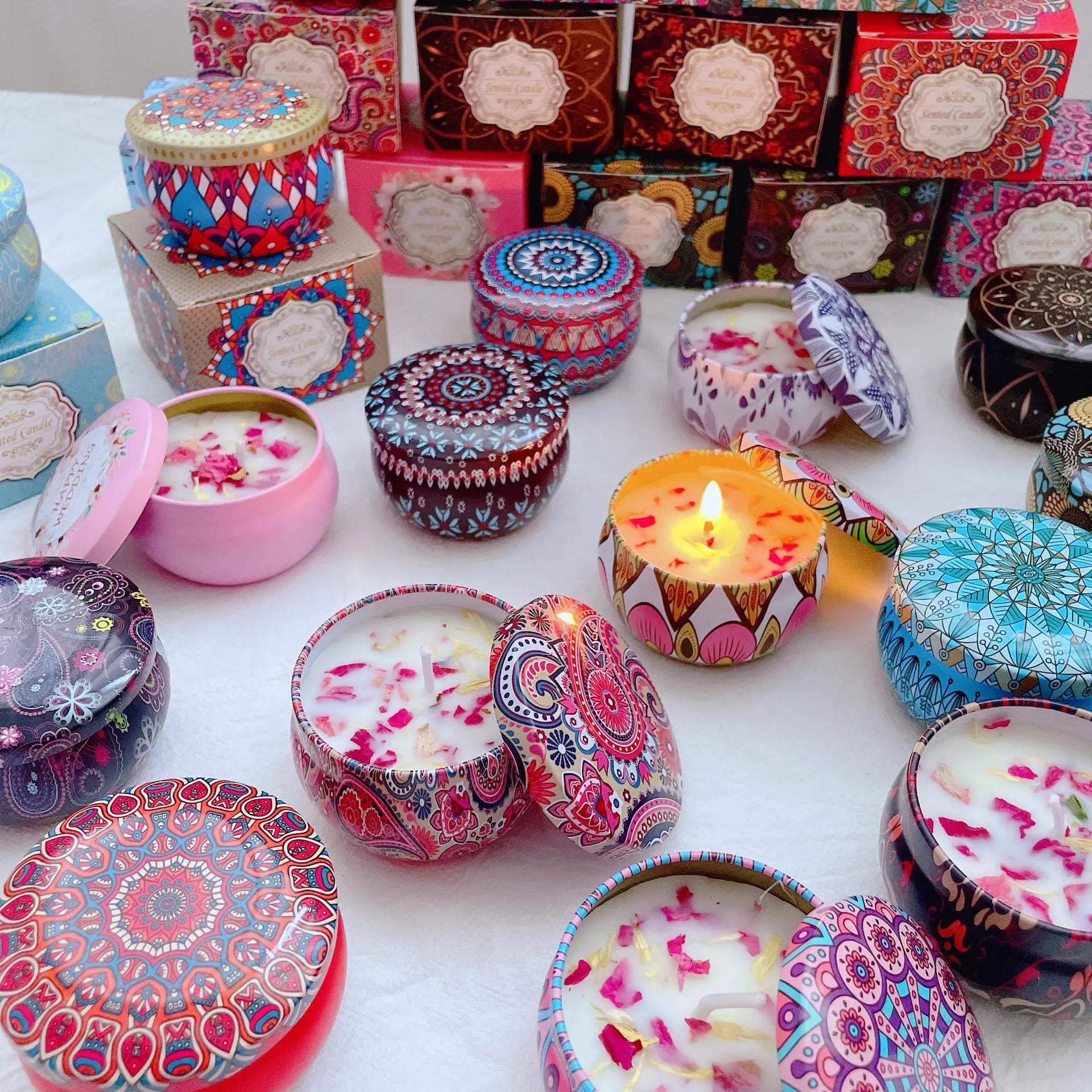 Assorted scented candles in colorful patterned metal tins with decorative floral petal wax and matching lids.