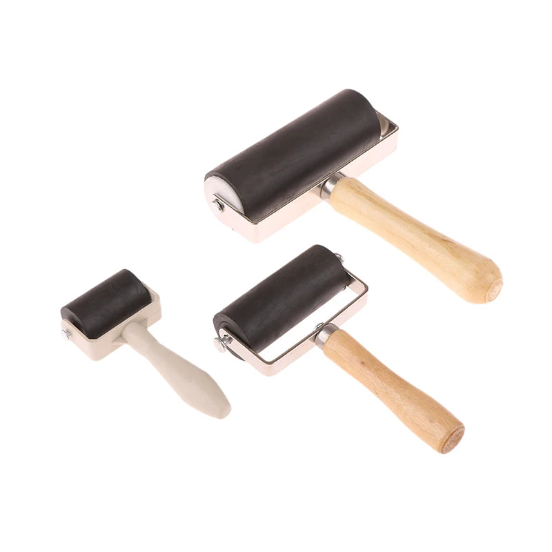 Three rubber brayer rollers of varying sizes with metal frames and light wooden handles against a white background.