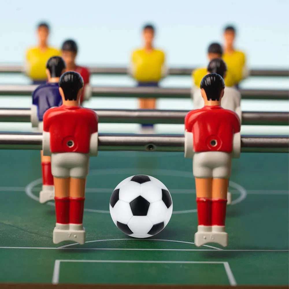 Table football game with red and yellow team players on metal rods and a classic black and white soccer ball.