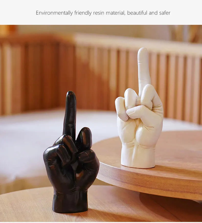 Black and white resin hand sculptures in a middle finger gesture, standing on a wooden table. Modern home decor.