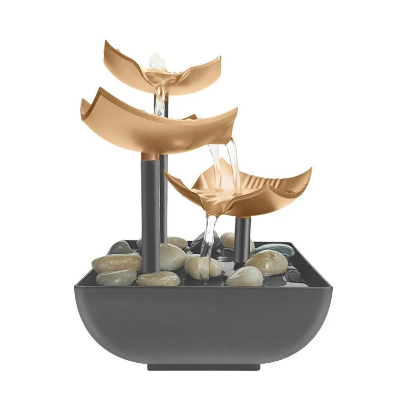 Three-tier gold-coloured tabletop water fountain with a grey basin and decorative smooth pebbles.