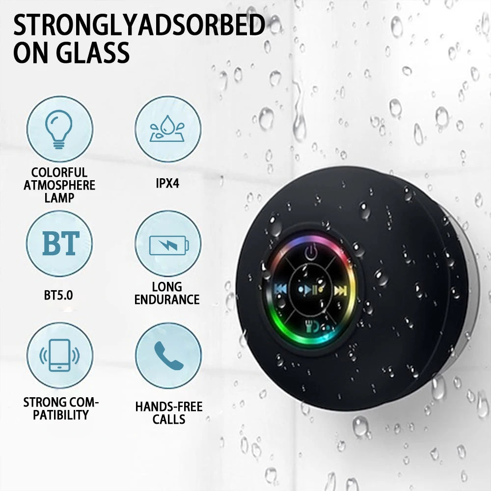 A black, circular waterproof Bluetooth shower speaker with a colourful LED ring, mounted on a wet glass surface.
