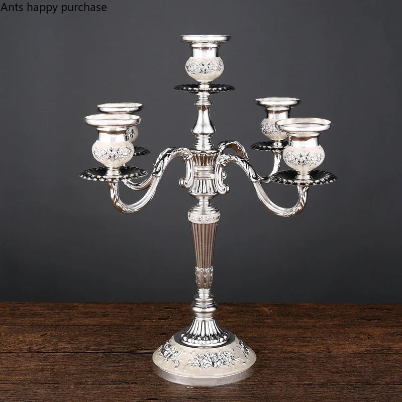 Silver European 5-arm candelabra with ornate floral detailing and cream-colored accents on a wooden table.