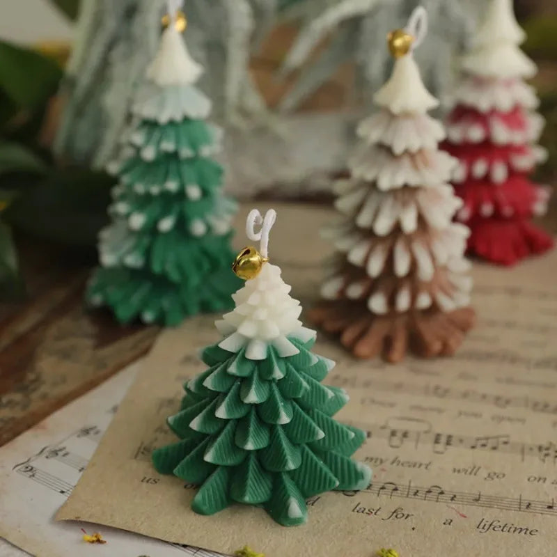 Festive Christmas tree-shaped candles in green, brown, and red, each topped with a delicate golden bell ornament.