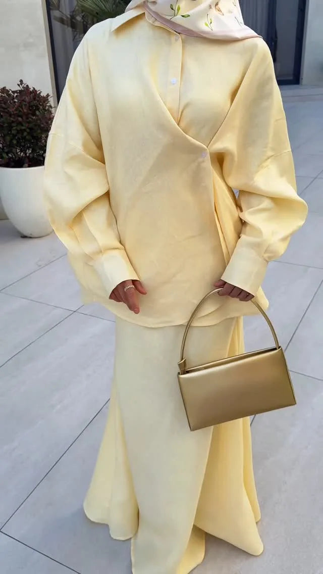 Soft yellow long-sleeve wrap shirt and matching maxi skirt set, paired with a sleek gold handbag.