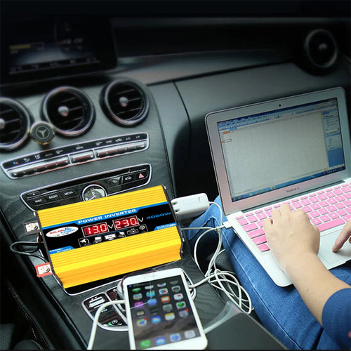 Yellow 4000W car power inverter with digital voltage display, powering a laptop and smartphone inside a vehicle.