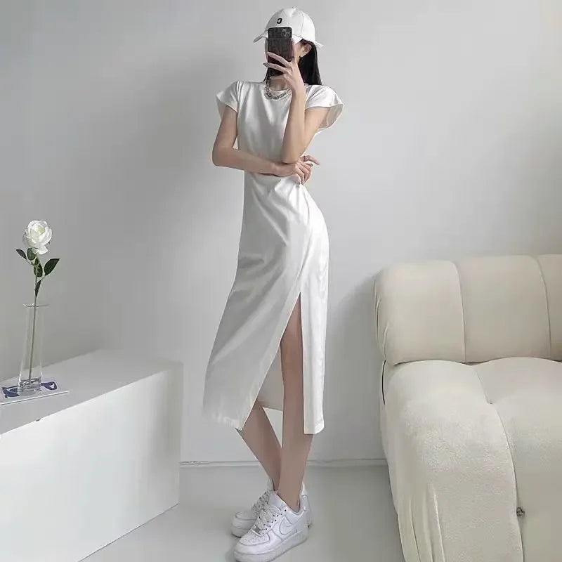 Woman wearing a white, short-sleeved midi dress with a high side slit, styled with a cap and trainers.