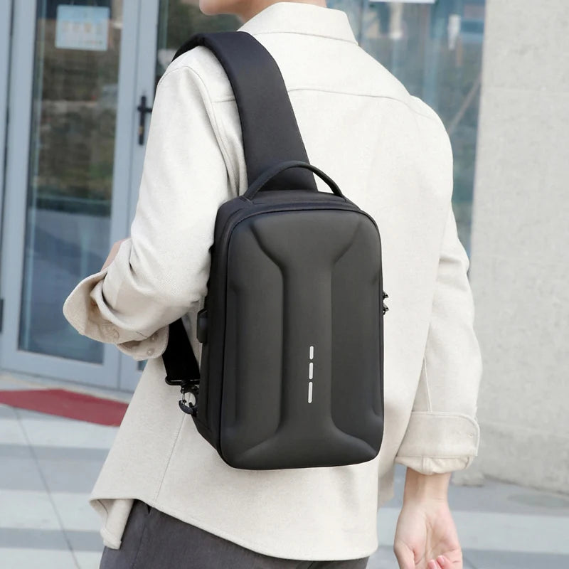 Black anti-theft crossbody bag with a sleek, moulded shell, top handle, and integrated USB charging port.