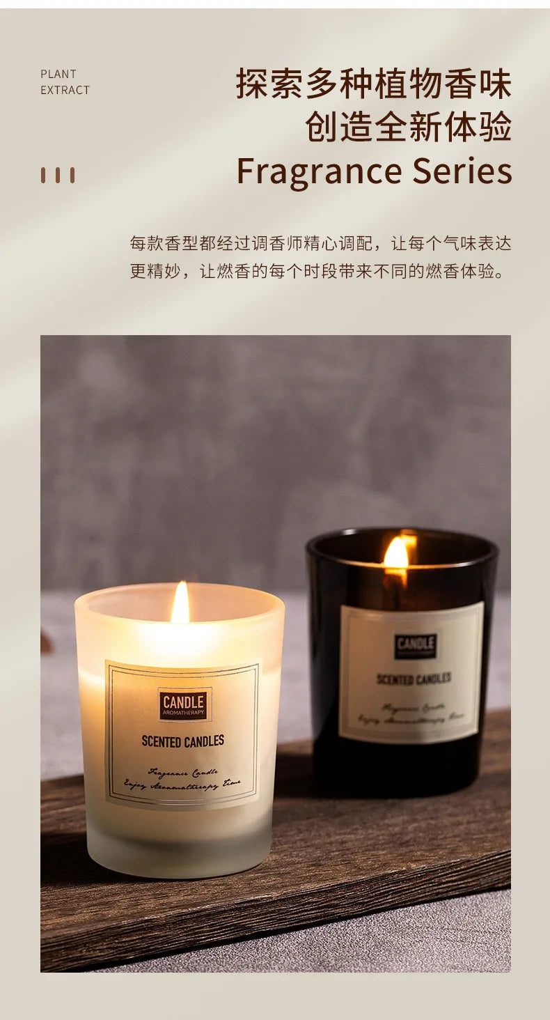 Two lit scented candles in matte frosted white and glossy black glass jars on a wooden surface.