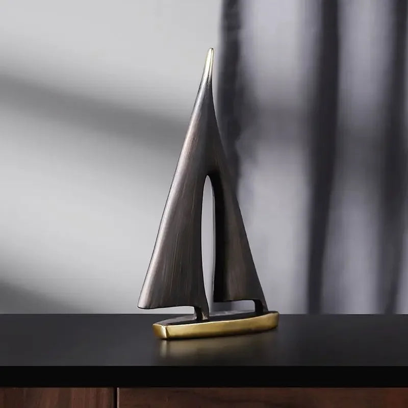 Elegant, minimalist sailboat ornament in brushed bronze with a polished gold base on a dark surface.