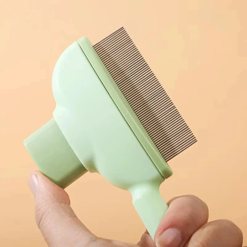 A hand holding a pastel green pet grooming comb with fine metal teeth, against a soft peach background.