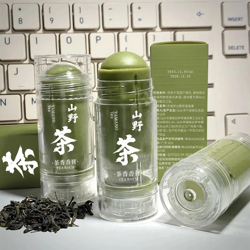 Green tea solid balm sticks in clear twist-up tubes with white Chinese text, alongside loose tea leaves and a box.
