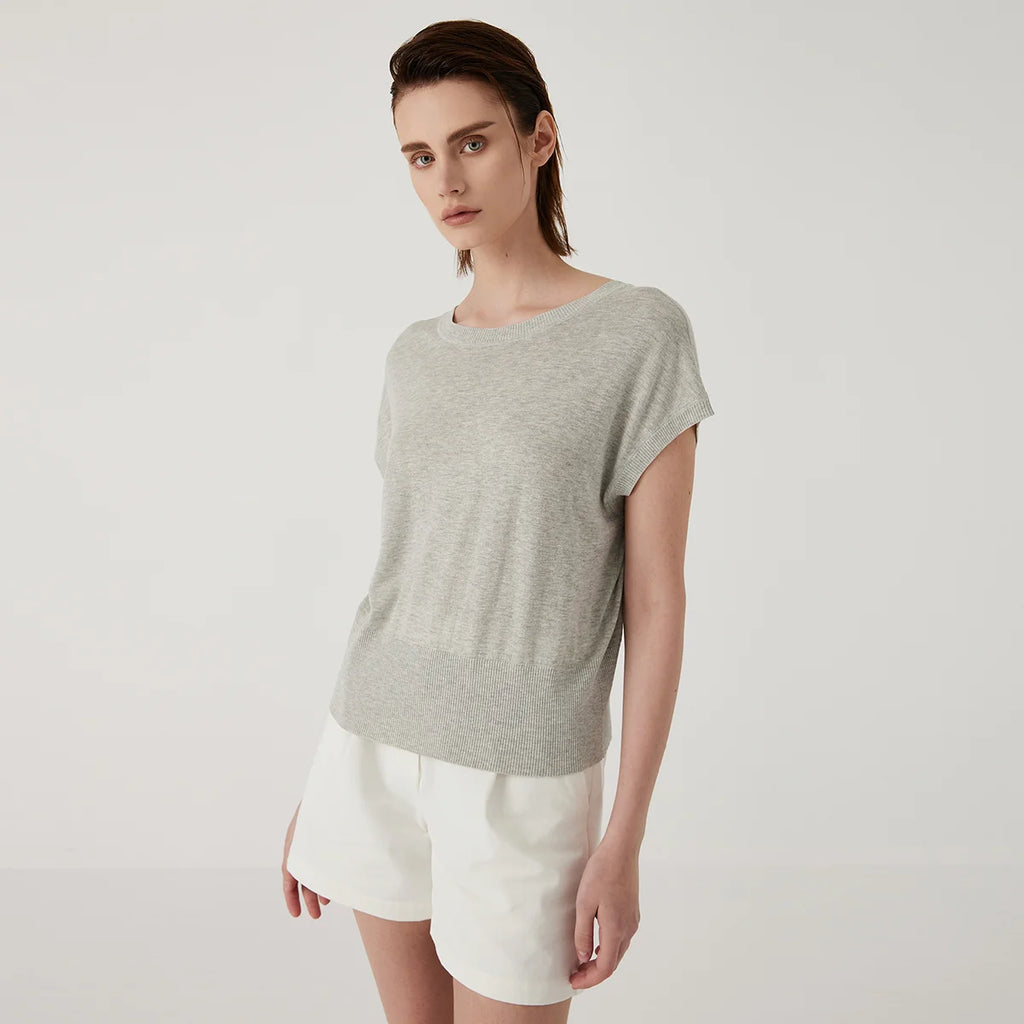 A model wears a light grey short-sleeved knit top with a ribbed hem and neckline, paired with white tailored shorts.