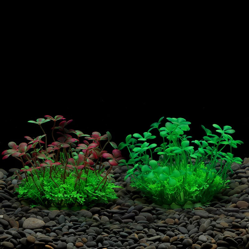 Two clusters of artificial clover-like aquarium plants, one red-tinged and one bright green, set on dark gravel.