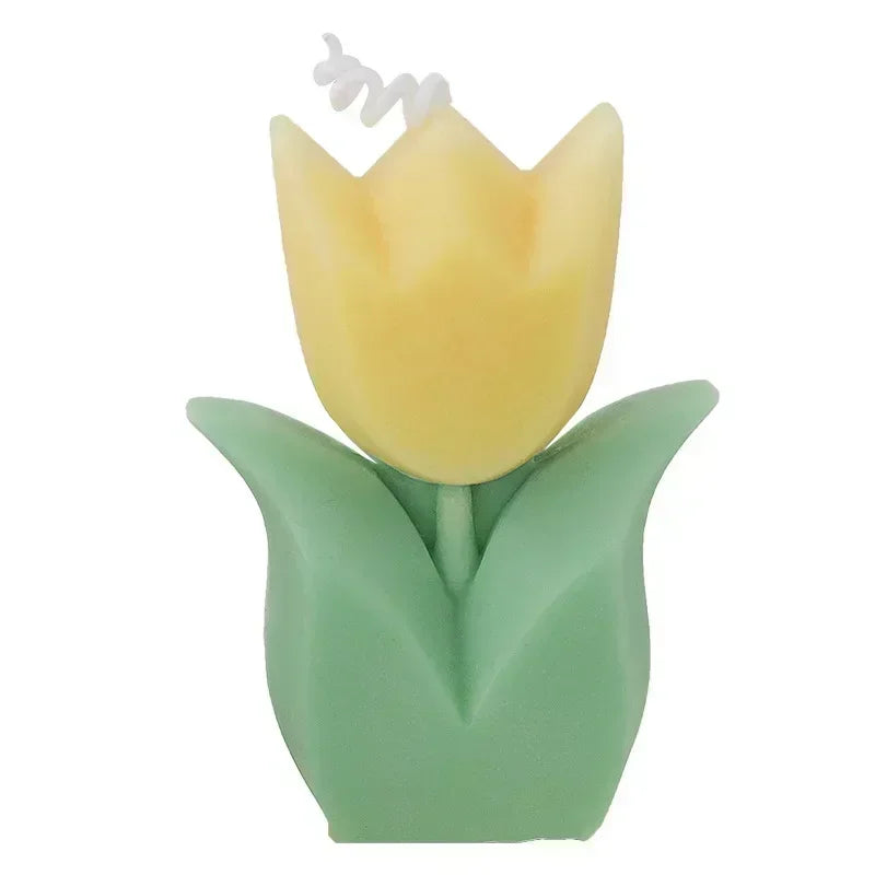 Decorative yellow tulip candle with green leaves and a white wick, isolated on a white background.