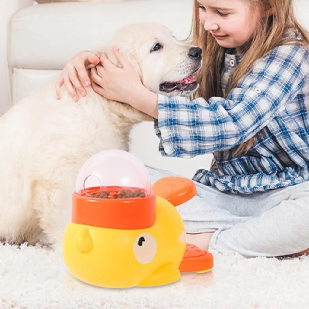 A yellow, whale-shaped interactive pet food dispenser with a clear dome top, resting on a white carpet.