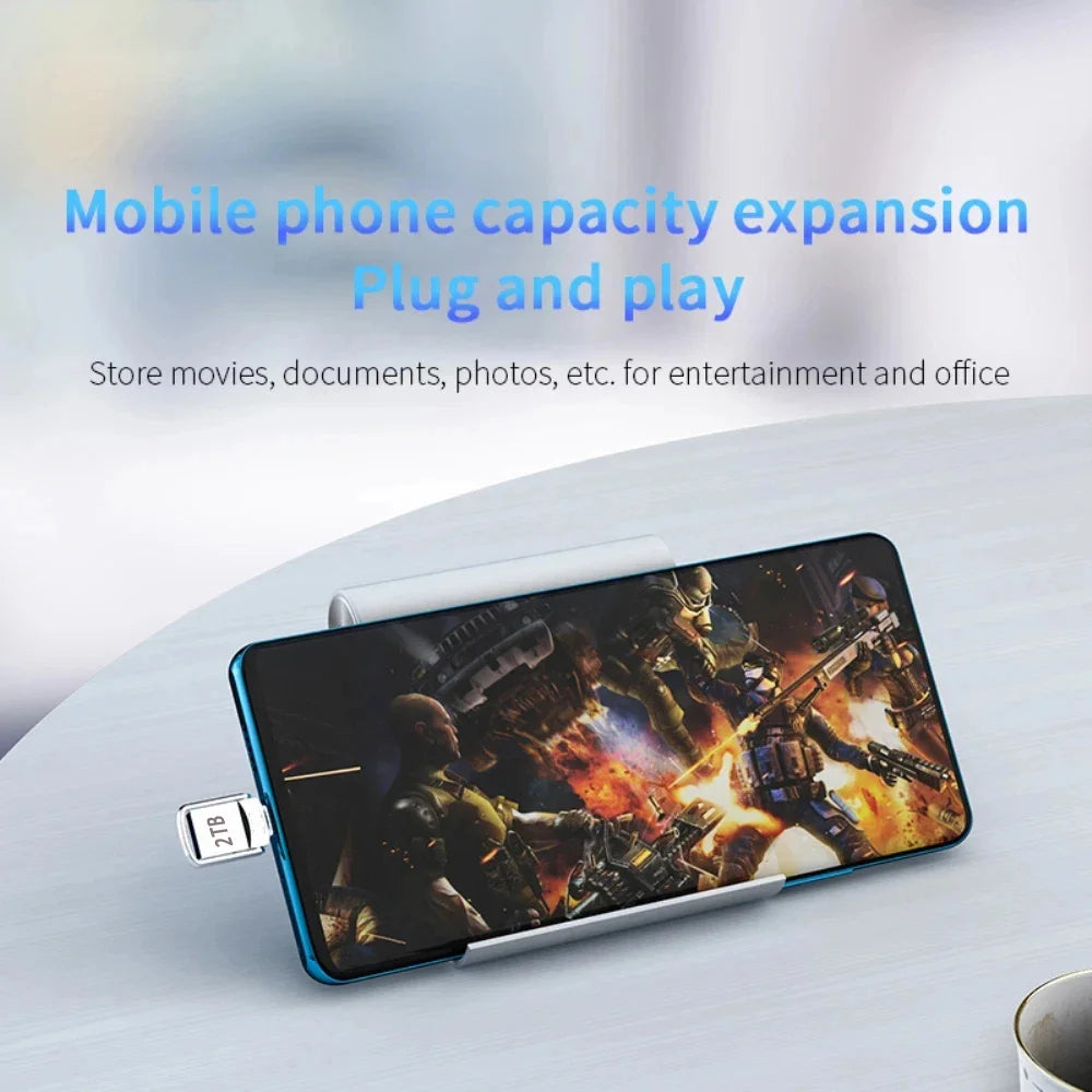 A sleek silver 2TB USB-C metal flash drive plugged into a smartphone displaying a video game.